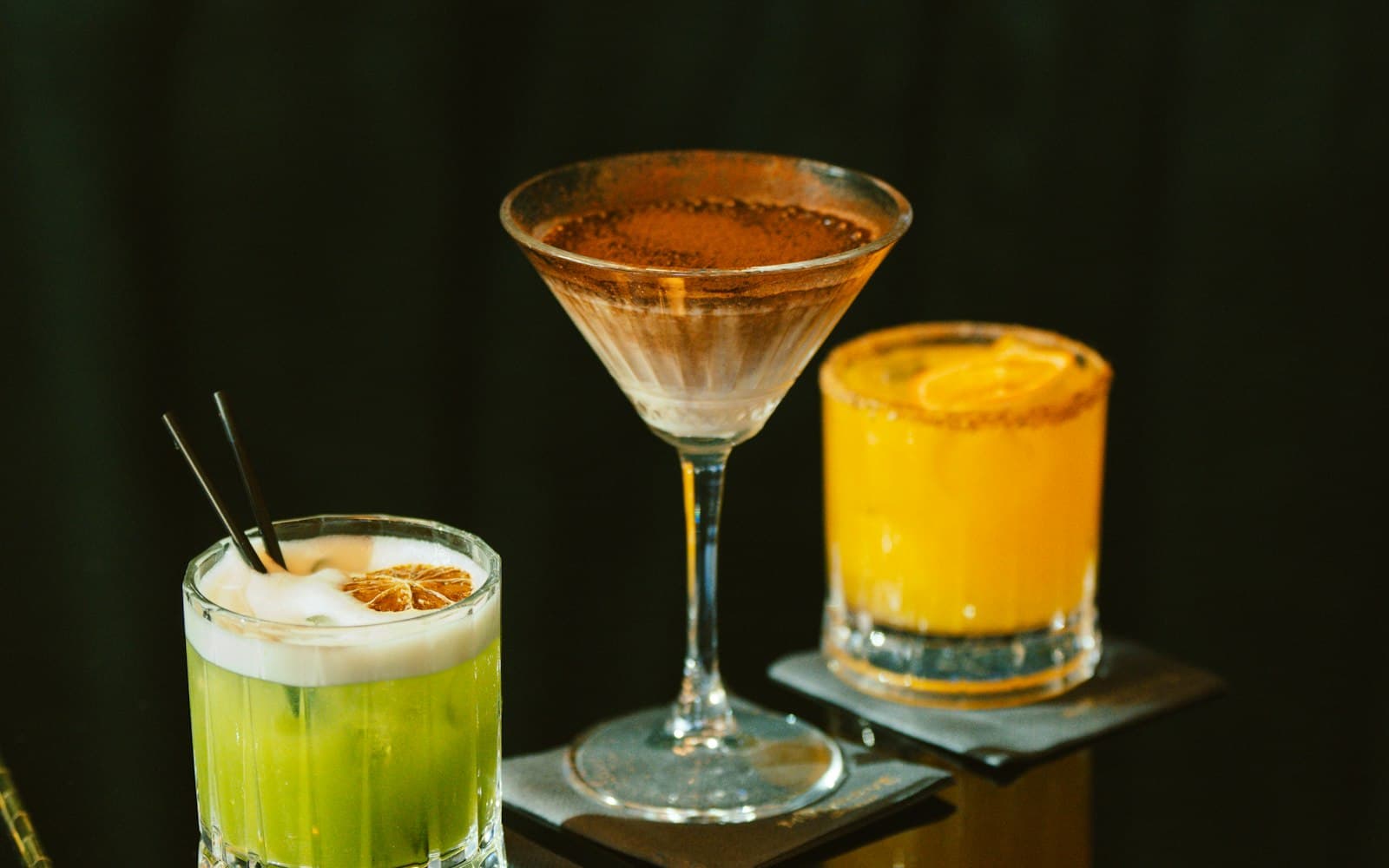 Three cocktails on a dark reflective bar top